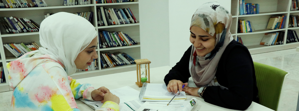 Two USAL students studying together in the university library, working on assignments and discussing in a collaborative environment.